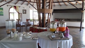 Un ricco buffet per la colazione con diversi cibi e bevande, tavoli con tovaglie bianche e travi a vista al soffitto.