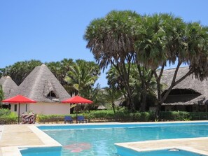 A pool area with thatched-roof structures and palm trees. - Olson Villa (Malindi)