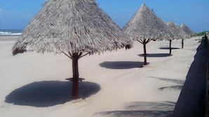 Una spiaggia con ombrelloni di paglia e un sentiero sabbioso.