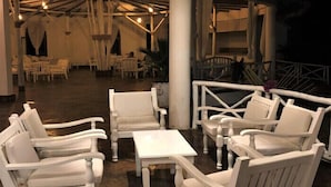 Un'ampia area interna con arredi bianchi, tra cui divani e un tavolino da caffè, illuminata da un lampadario.