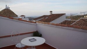 Une terrasse sur le toit, avec une table ronde et des chaises en métal, offrant une vue sur le paysage urbain et ses toits traditionnels recouverts de tuiles.