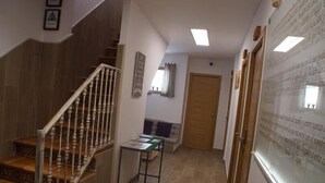Un escalier avec des marches en bois et une rampe blanche, menant à un palier où se trouvent une petite table et un banc.