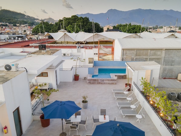 Enjoy panoramic views of the city and mountains from this rooftop space, featuring a pool, seating area, and lush greenery.