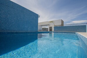 Relax by the pool surrounded by a geometric patterned wall and a small tree with vibrant flowers.