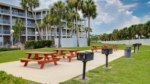 Un hotel con varios pisos, mesas de picnic al aire libre y un estacionamiento cercado.