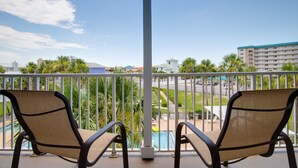 Un balcon avec deux fauteuils en osier, une piscine et une vue sur une route et des immeubles.