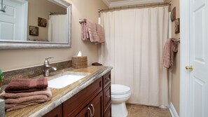 Un baño con lavamanos, espejo e inodoro. Hay toallas y una cesta en la encimera.