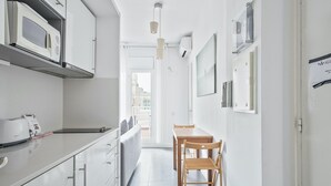 Ett smalt kök med vita skåp, en mikrovågsugn och en matplats med ett träbord och stolar.