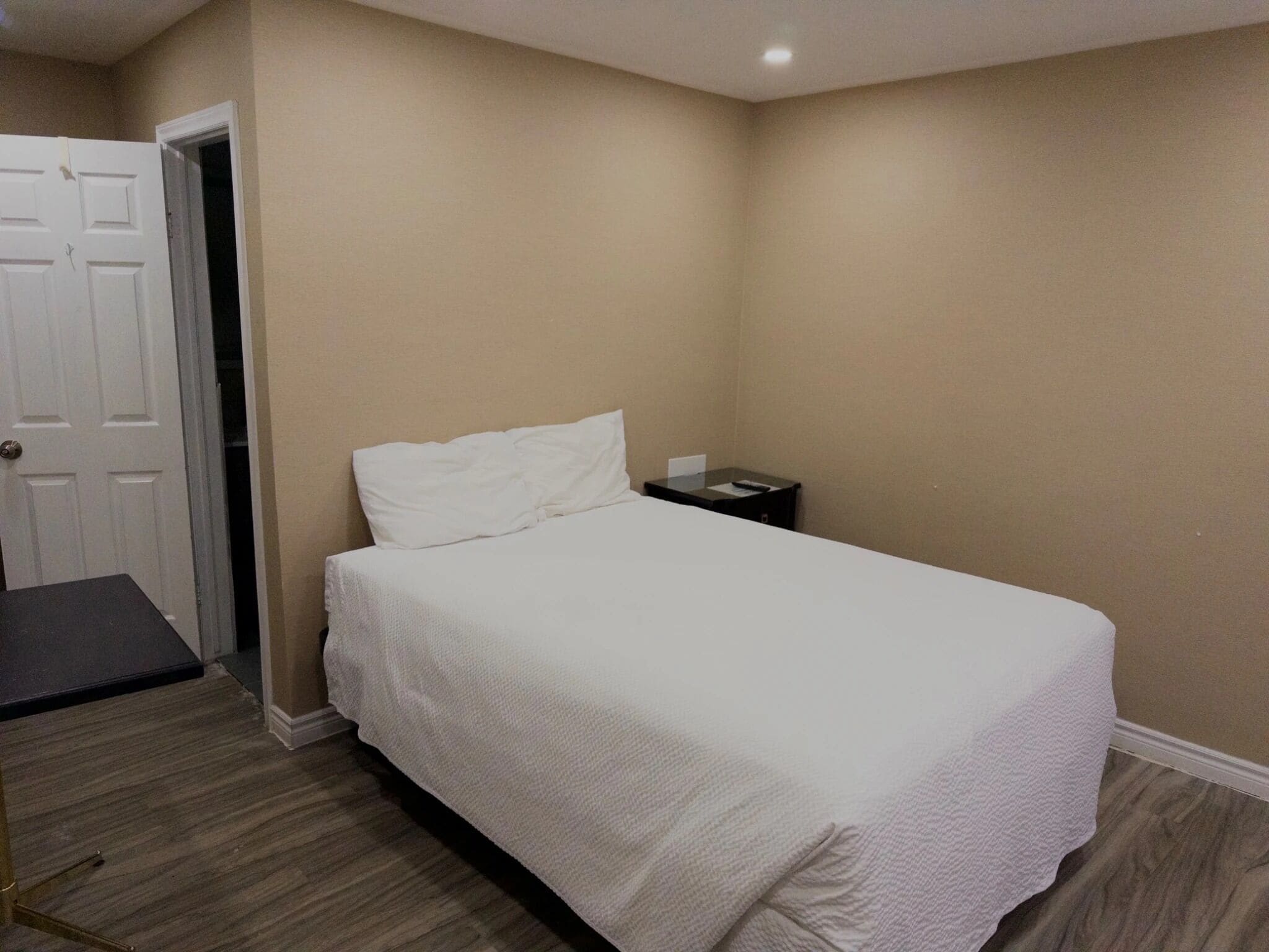 A bedroom with a bed, a nightstand, a door, and a small table.