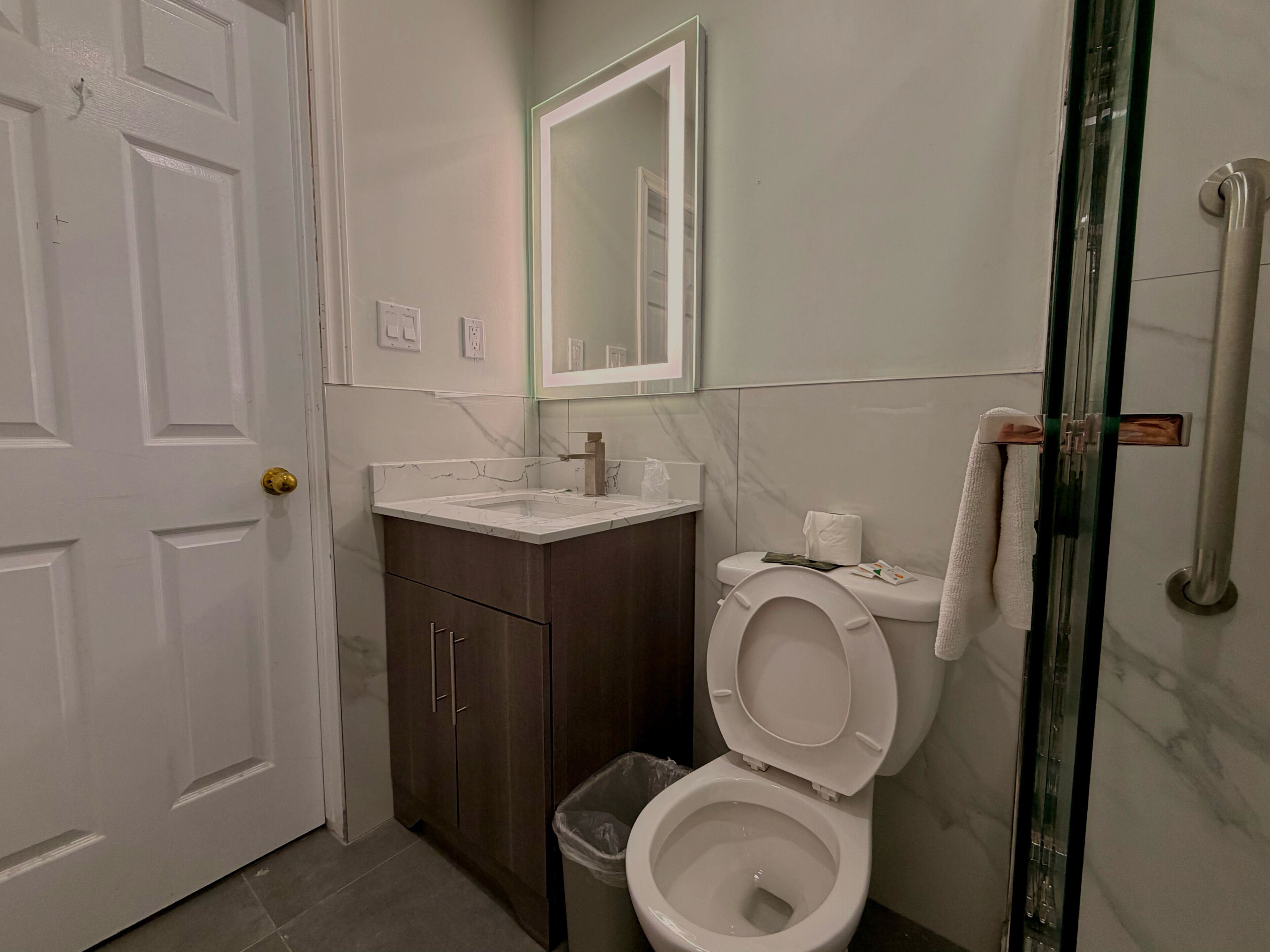 A bathroom with a toilet, sink, mirror, and glass shower enclosure.