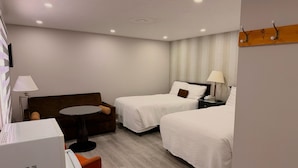 A hotel room with two beds, a sofa, a small table, a lamp, and a TV.