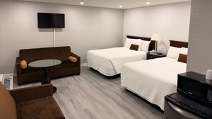 A hotel room with two beds, a sofa, a TV, a lamp, and a microwave.