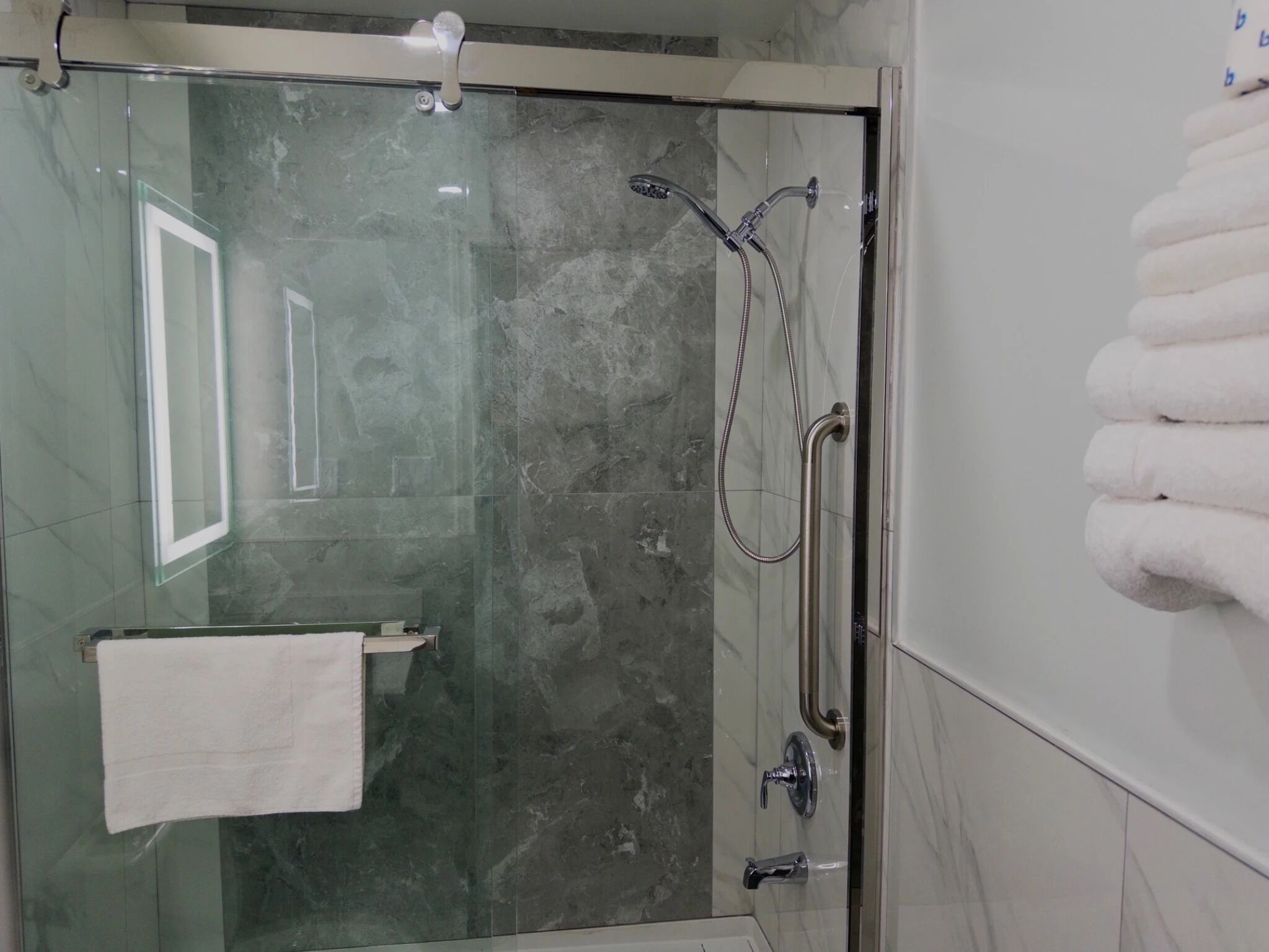 A glass-enclosed shower with a handheld showerhead and a handheld faucet.