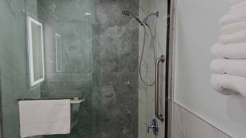 A glass-enclosed shower with a handheld showerhead and a handheld faucet.
