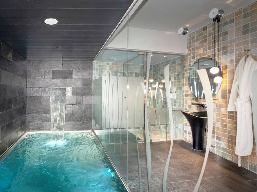 Un baño moderno con un jacuzzi de vidrio, cabina de ducha con mampara de vidrio y una bata blanca colgada en la pared.
