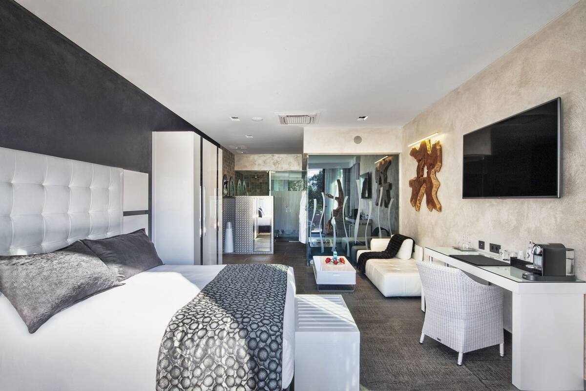 A modern hotel room with a large bed, a desk, a seating area, and a TV.