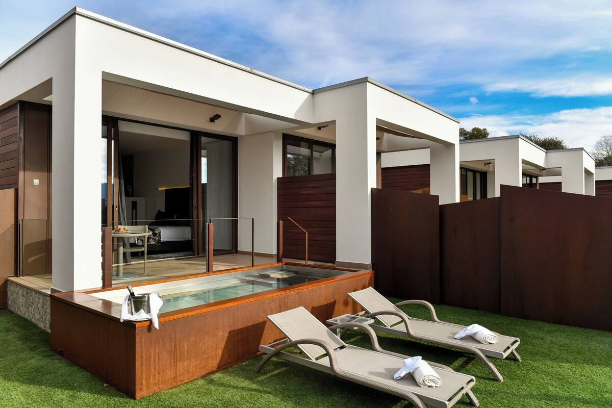 A modern outdoor pool area with lounge chairs and a glass-enclosed spa room.