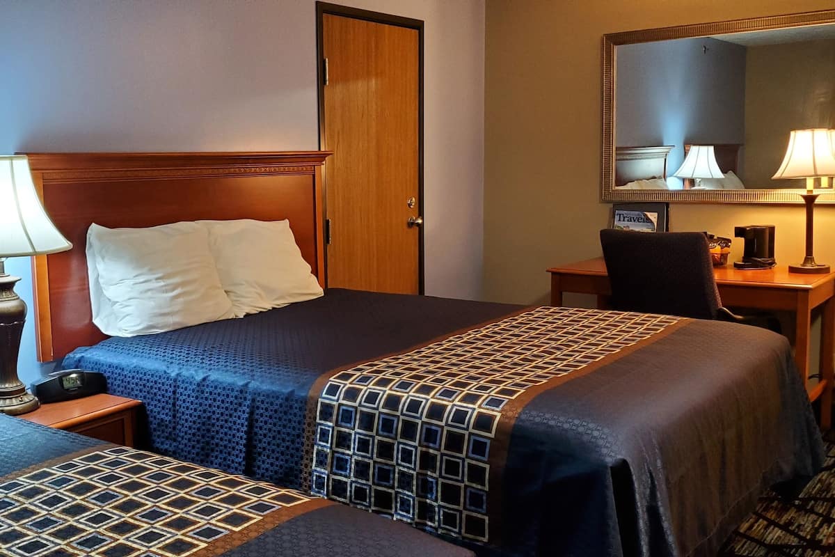 Habitación de hotel con dos camas, cabecero de madera, escritorio con silla, espejo y lámpara.