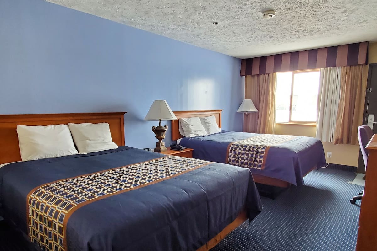 Habitación de hotel con dos camas, un escritorio, una silla y una ventana con cortinas.