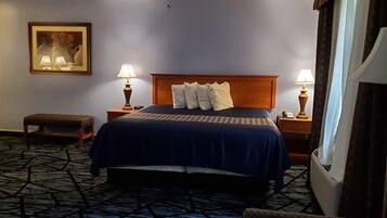 A hotel room with a large bed, two bedside tables with lamps, a bench, a framed picture on the wall, and a window with curtains.
