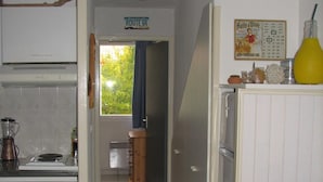 A compact kitchen with a stove, blender, and a wooden cabinet. A dining area with a sofa and a vase of flowers is visible. A sign reading "ROUTE 66" is on the wall. - Apartment with garden (Carcans Plage)
