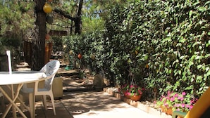 An outdoor patio with a table and chairs, surrounded by lush greenery and flowering plants. - Apartment with garden (Carcans Plage)