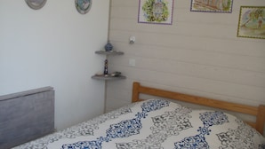 A bedroom with a bed, a small shelf with decorative items, and three wall-mounted pictures. - Apartment with garden (Carcans Plage)