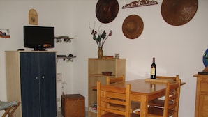A dining area with a wooden table and chairs, a television on a cabinet, and a vase with flowers on a shelf. - Apartment with garden (Carcans Plage)