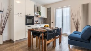A modern kitchen with white cabinets, a built-in oven, and a dining area with a wooden table and chairs. - Residence "La Pergola" central area, garden, swimming pool, parking (Malcesine)