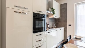 A modern kitchen with white cabinetry, a built-in oven, and a sink. - Residence "La Pergola" central area, garden, swimming pool, parking (Malcesine)