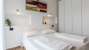 A modern bedroom with a large bed, white bedding, a wall-mounted abstract painting, and built-in wardrobe. - Residence "La Pergola" central area, garden, swimming pool, parking (Malcesine)