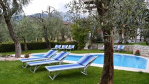A pool area with lounge chairs and a stone wall. - Residence "La Pergola" central area, garden, swimming pool, parking (Malcesine)