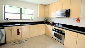 Una cucina con mobili chiari, un piano di lavoro nero, un forno a microonde, un forno e una finestra con piante all'esterno.