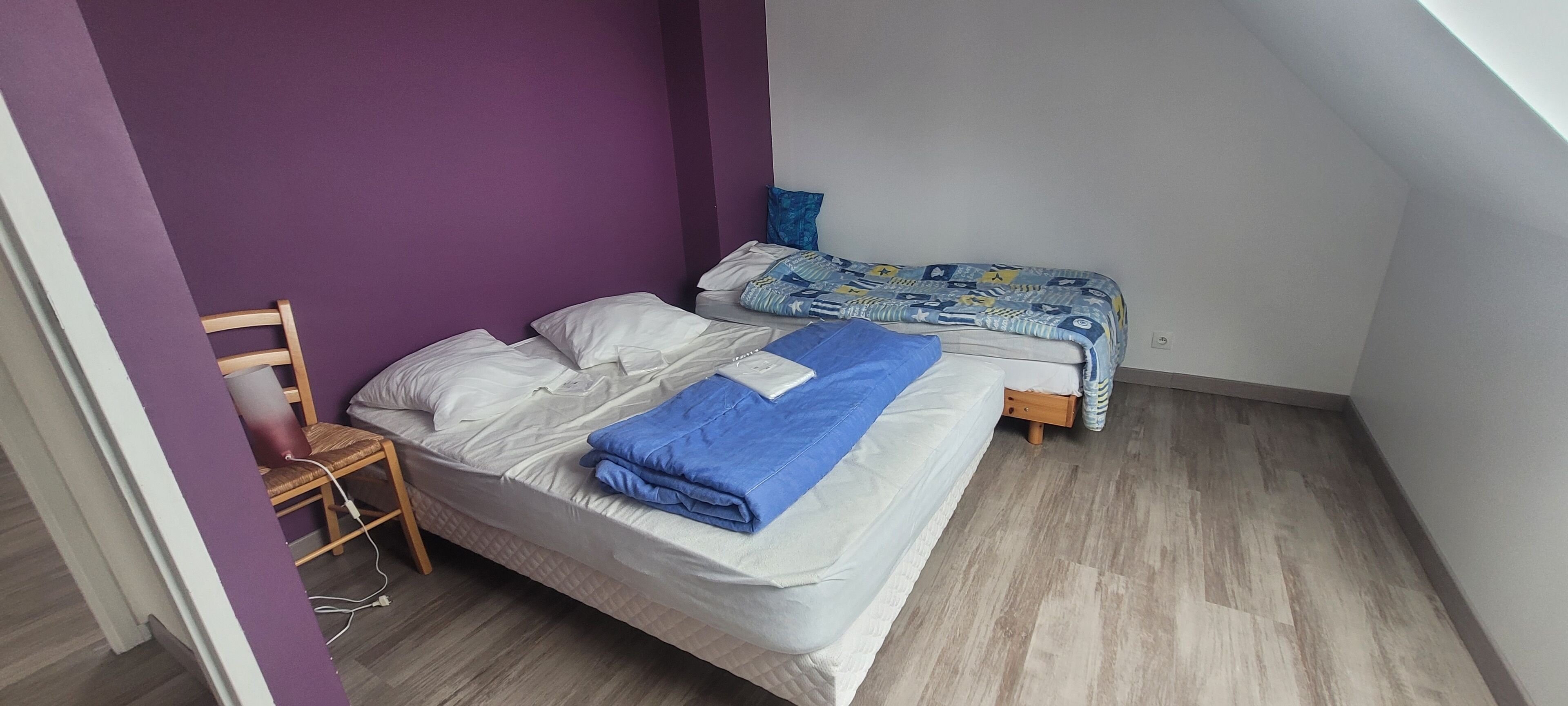 A bedroom with two beds, purple walls, and a wooden floor.