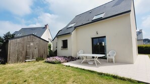A modern house with a patio, a wooden shed, and a garden with flowers.