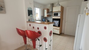 A kitchen with a microwave, oven, and a refrigerator. There is a wooden counter with a sink and a red chair.