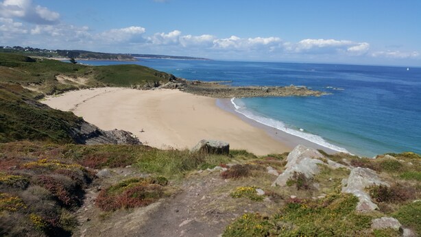 A coastal landscape with a sandy beach, rocky outcrops, and a clear view of the ocean.