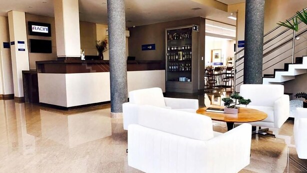 A modern lobby with a reception desk, white sofas, a coffee table, and a staircase.