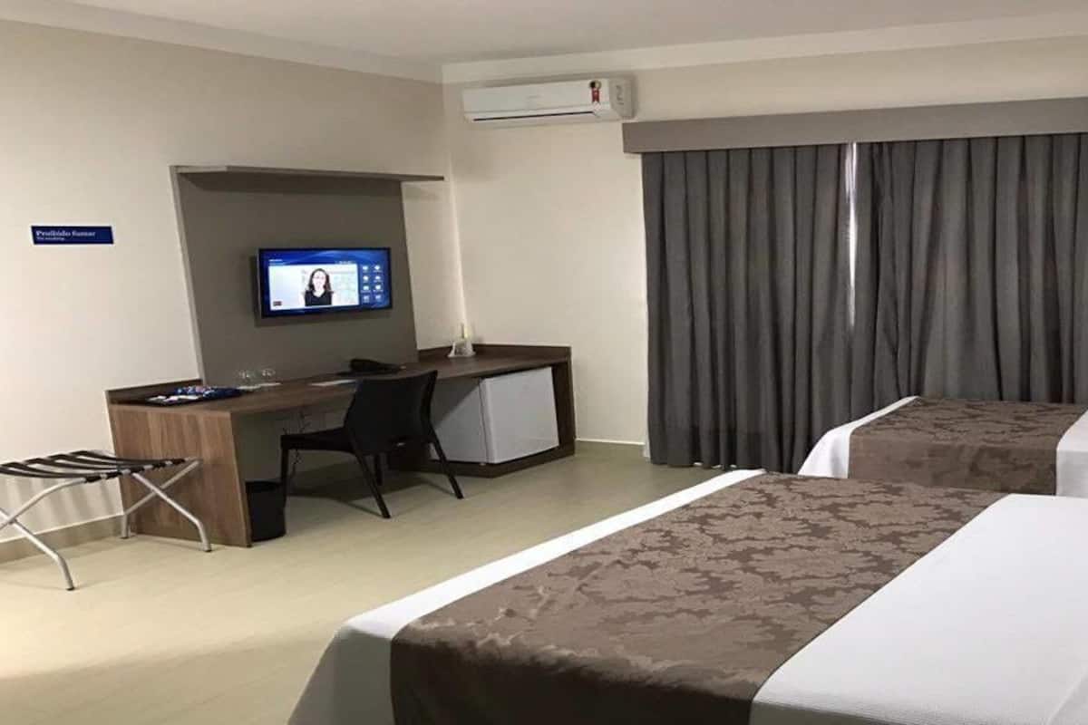 Una habitación de hotel con dos camas, un escritorio con una computadora, una silla y un televisor.