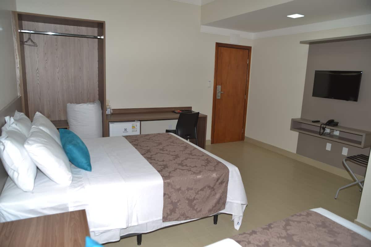 Una habitación de hotel con cama, escritorio, silla, televisor y armario.