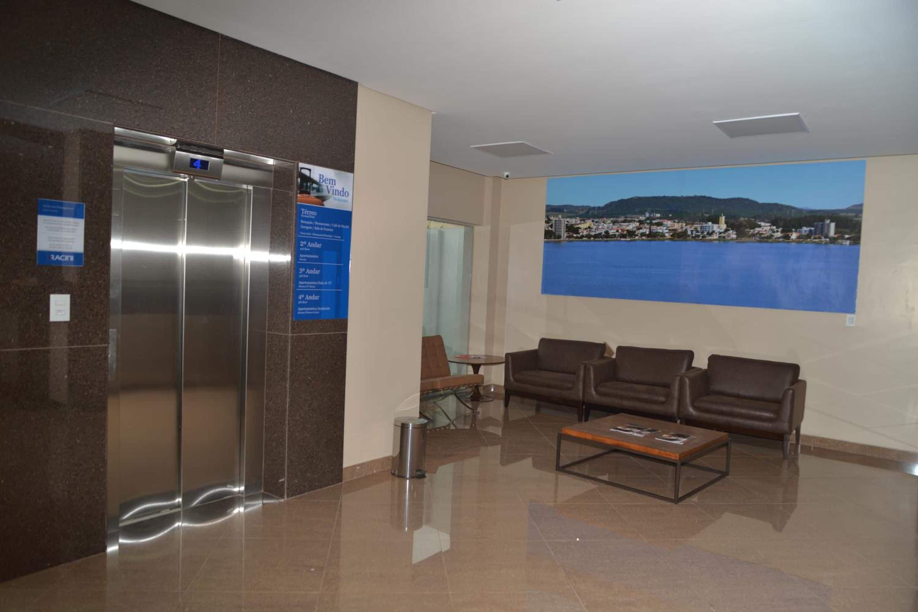 A lobby with a reception desk, a digital clock, a large window with a cityscape view, and a seating area with sofas.