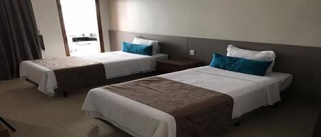 Una habitación de hotel con dos camas individuales, una mesita de noche y un ventanal grande.
