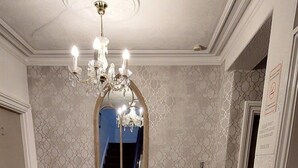 Un couloir avec un tapis rouge, un banc en bois, un lustre, un miroir et un radiateur.