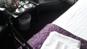 Une chambre d’hôtel avec un lit, une chaise, une petite table avec une théière, des tasses et des en-cas, une table de chevet avec une lampe et un panneau de bienvenue.