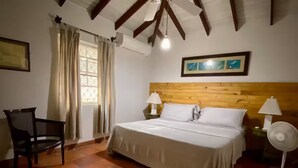 Ein Schlafzimmer mit einem Holz-Kopfteil, einem Bett mit weißer Bettwäsche, einem Sessel, einem Nachttisch mit Lampe und einer Wand-Klimaanlage.