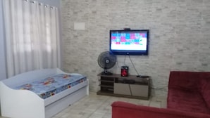 A living room with a bed, a TV mounted on the wall, a fan, and a red chair. - Sítio em Araçoiaba da Serra (Araçoiaba da Serra)