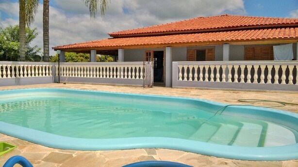 A swimming pool with a tiled deck, a covered patio, and a white fence with decorative balustrades. - Sítio em Araçoiaba da Serra (Araçoiaba da Serra)