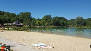 Une plage de sable avec un lac, des arbres et un b âtiment doté d’un toit en pente.