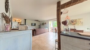 Un grand espace de vie comprenant un canapé, une table basse et un téléviseur. Il y a également un coin cuisine avec un plan de travail et un luminaire suspendu.