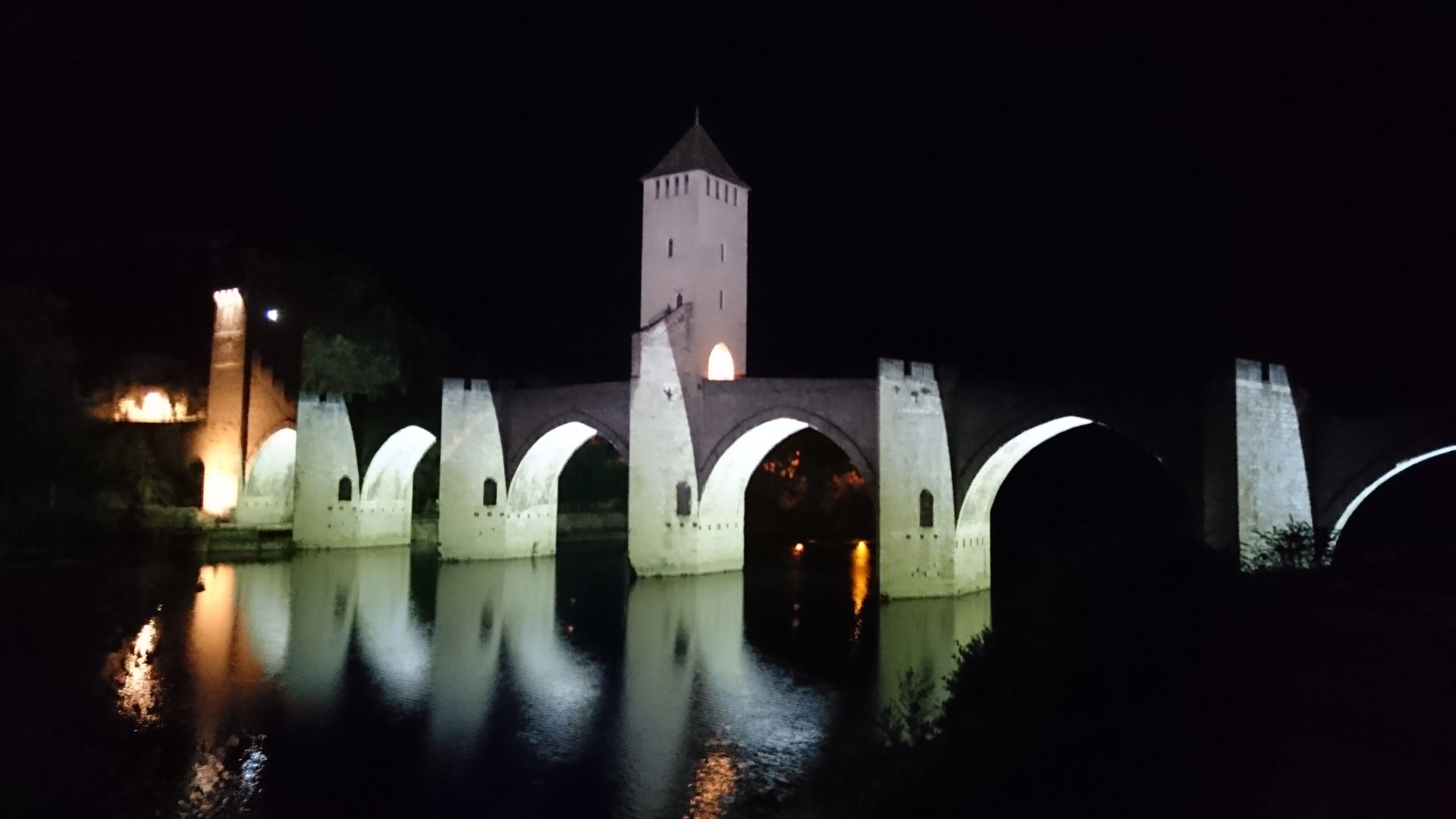A historic bridge with multiple arches and a tower, reflecting in the water below.